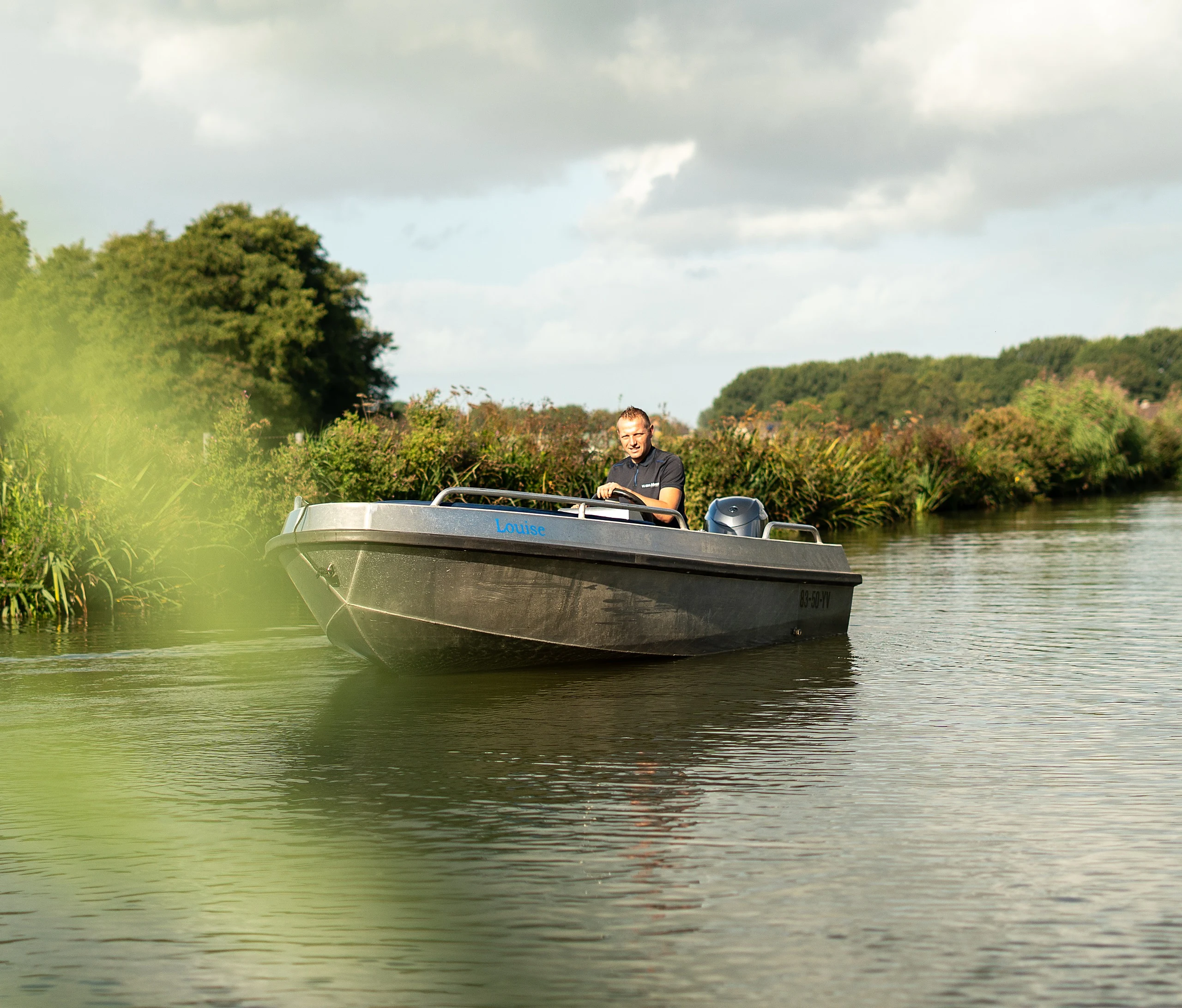 Aluminium werkboot Louise vaart langs een rietoever, met een schipper achter het stuur