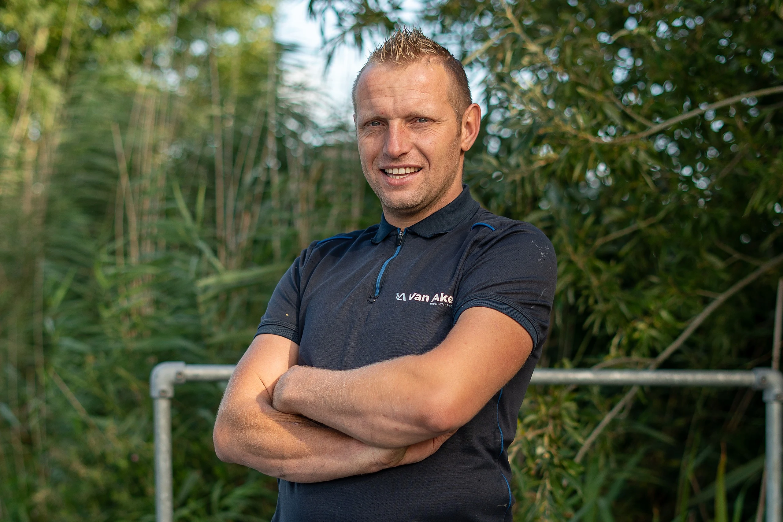 Portret van Nico van Aken in een donkerblauwe polo met het Van Aken logo, armen over elkaar, voor een rietkraag